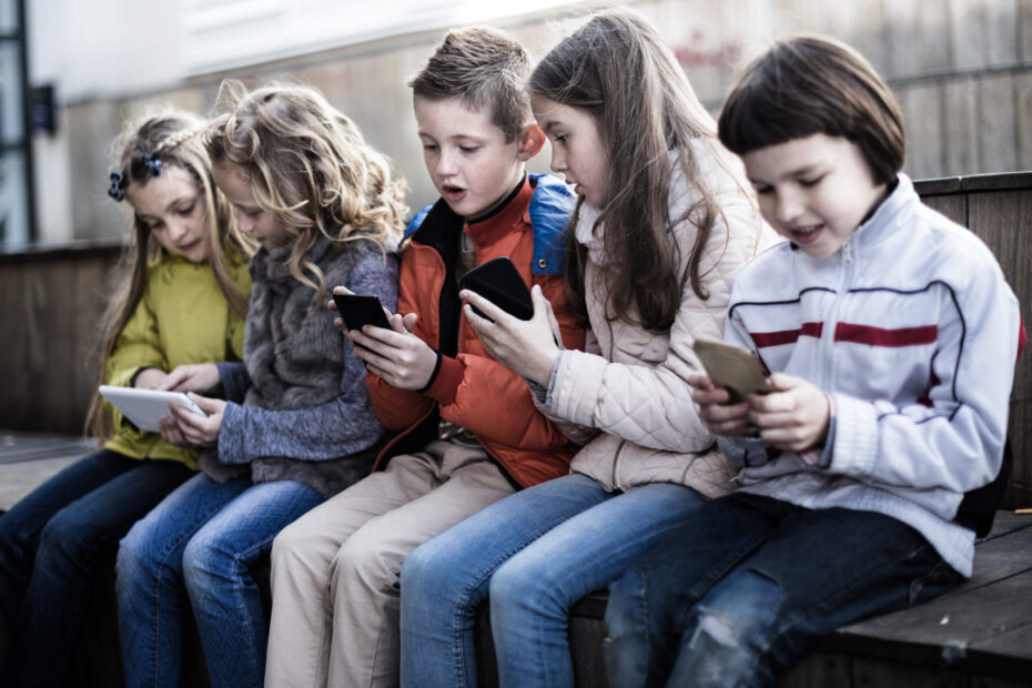modern ordinary children playing with the phone on bench outdoors
