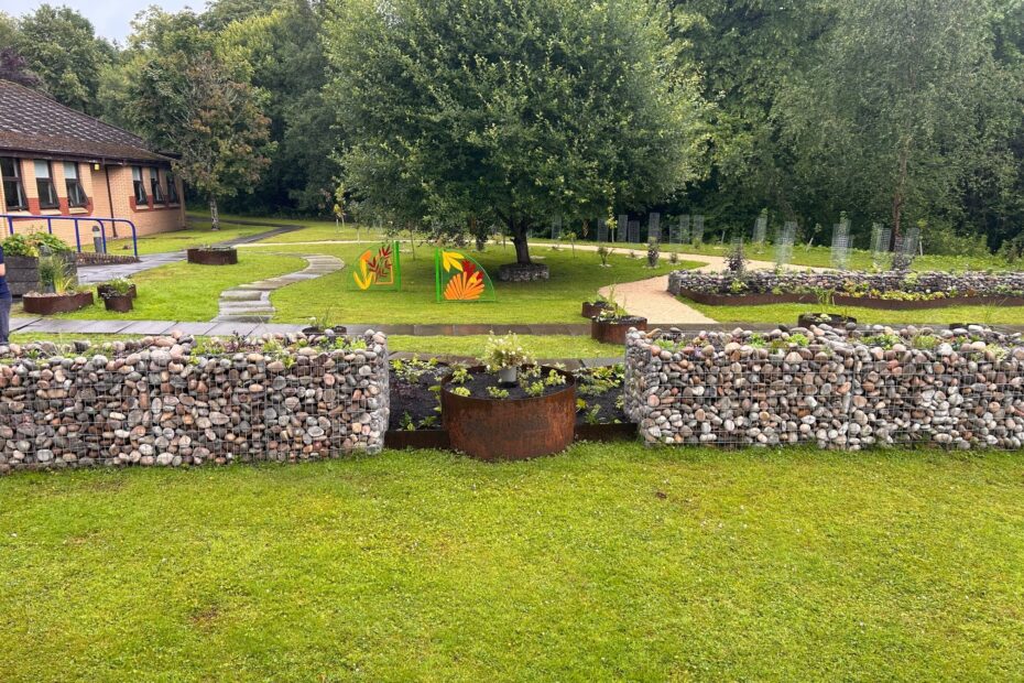picture of Kyle unit garden at Ailsa Hospital with pebble raised plant beds, tree and artwork panels.