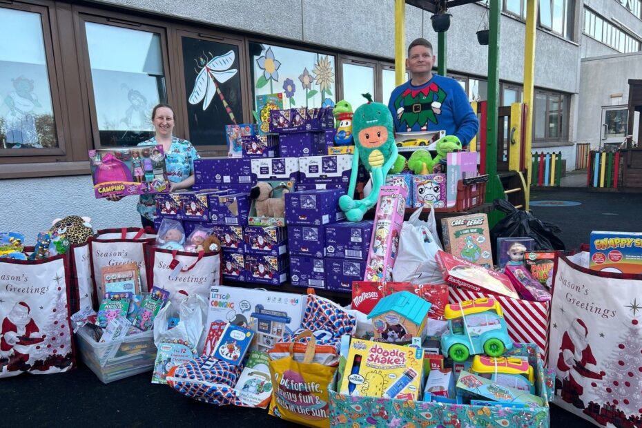 Michelle, play leader and Michael pictured standing outside in play ground behind lots of toys and selection boxes.