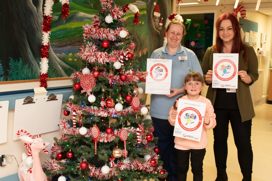 Michelle and Kayleigh standing in the ward with competition winner Darcie in front of the ward Christmas tree. Darcie is holding her winning entry picture.
