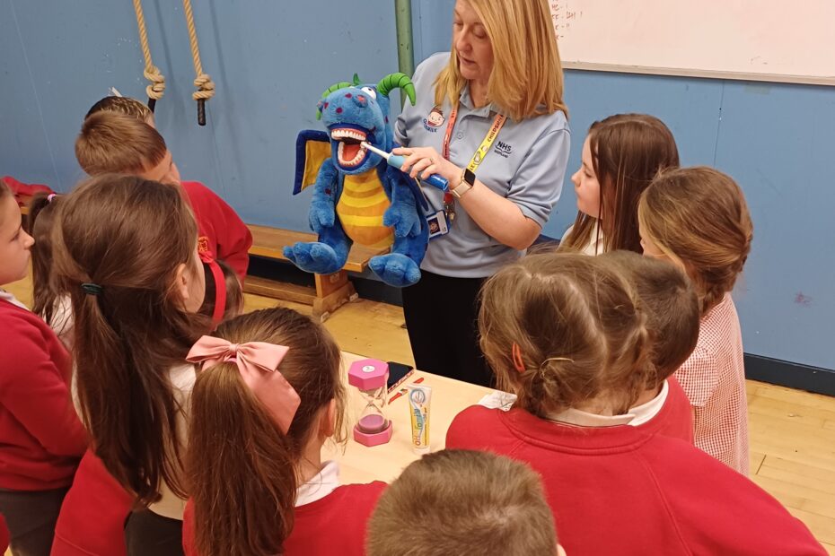Member of staff demonstrating tooth brushing to a group of primary aged children