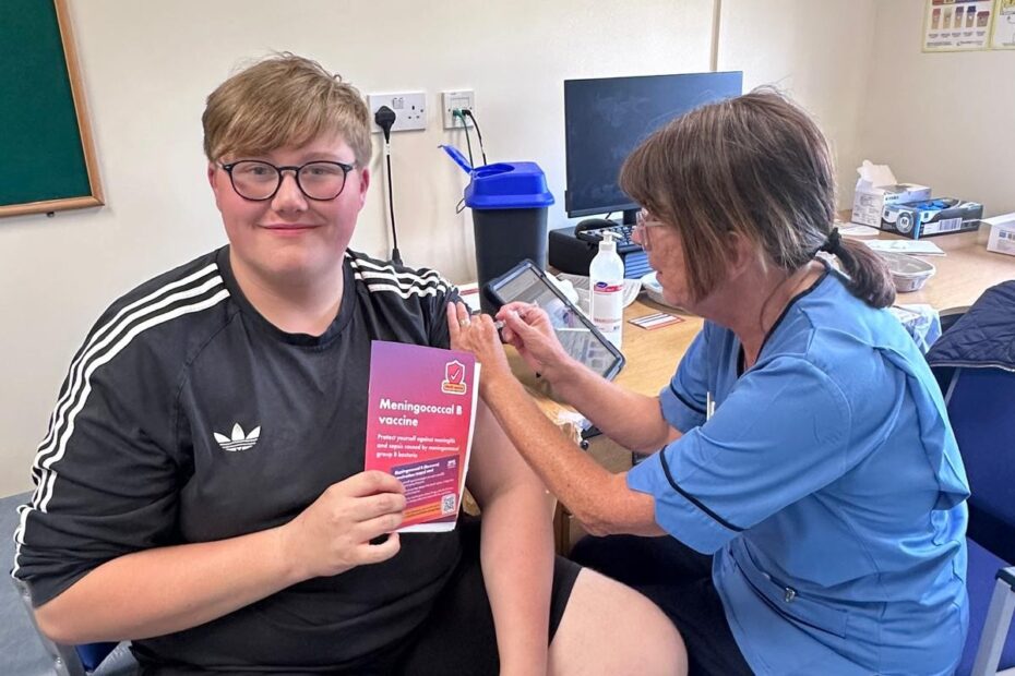 Patient sitting getting their MenB vaccine by clinician in clinical room.