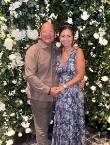 Charles “Chick” Hamilton with his wife in front of wall of white flowers.