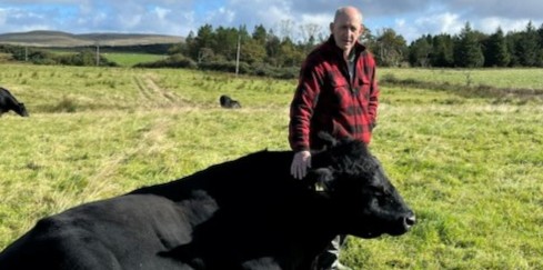 Willie McAllister stoking a large black bull in a field.